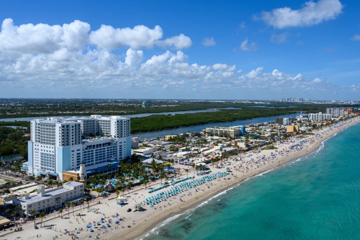 Aerial view of a beach with hotels and turquoise water on a sunny day.