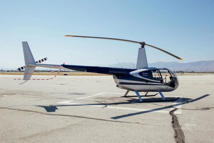 Blue and white helicopter parked on an airport tarmac with mountains in the background.