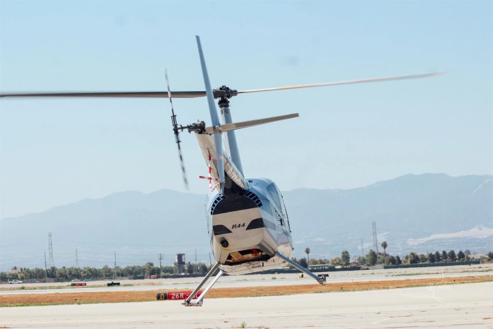 Helicopter taking off from runway with mountains in background.