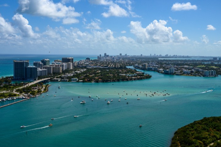 Aerial view of a city skyline with waterways, boats, and skyscrapers under a blue sky.
