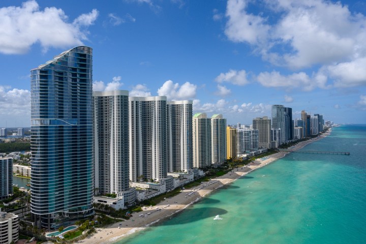 Tall beachfront skyscrapers with ocean and bright sky.