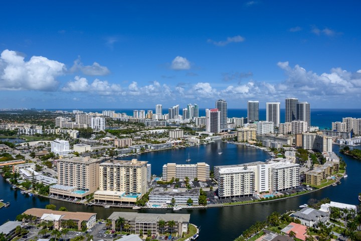 Aerial view of coastal city with tall buildings and a body of water under a clear blue sky.
