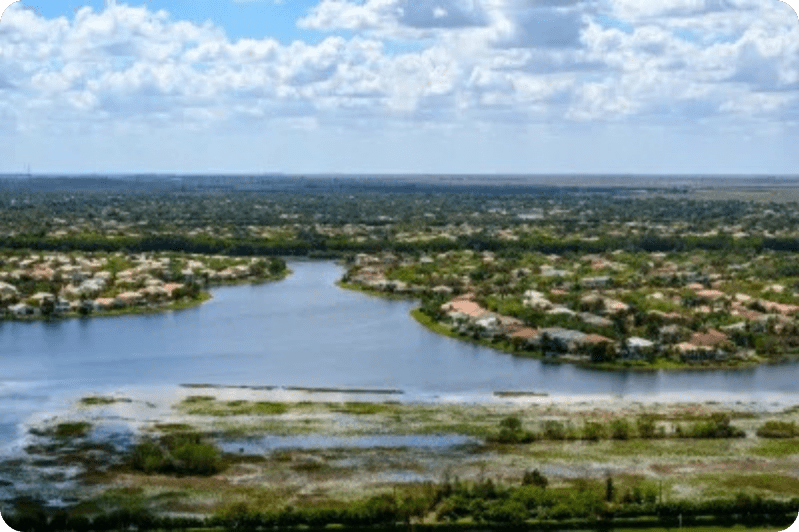 Aerial view of a lake with surrounding houses and clouds in the sky.