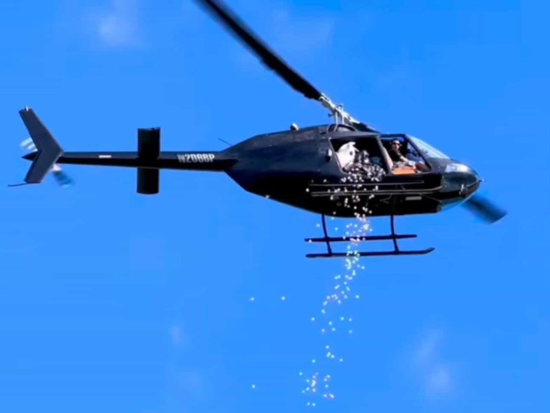 Helicopter flying in blue sky releasing small objects downward.
