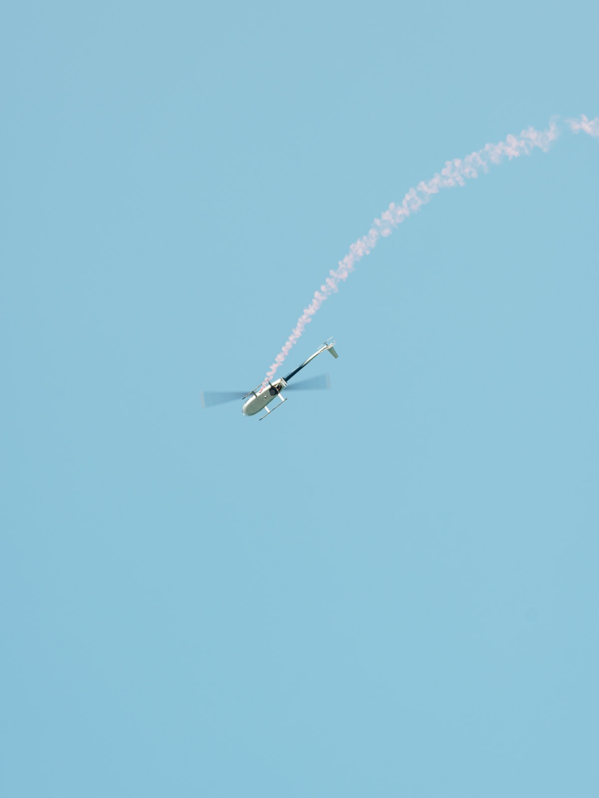Helicopter flying with smoke trail against a clear blue sky.