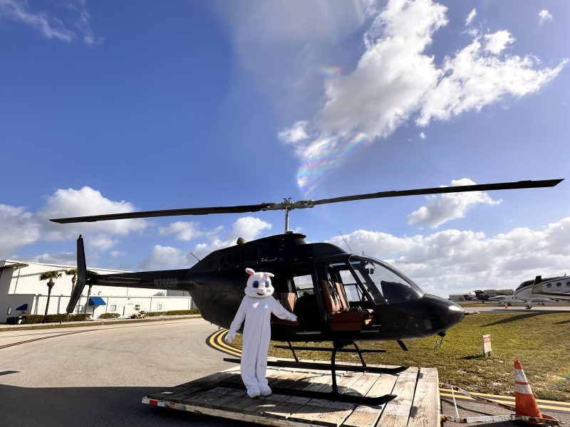Person in white bear costume stands by a black helicopter on a sunny day.