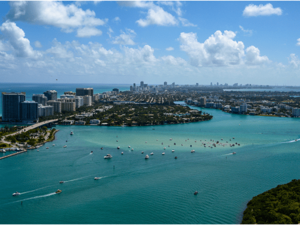 Aerial view of city skyline with blue water and boats, under a partly cloudy sky.
