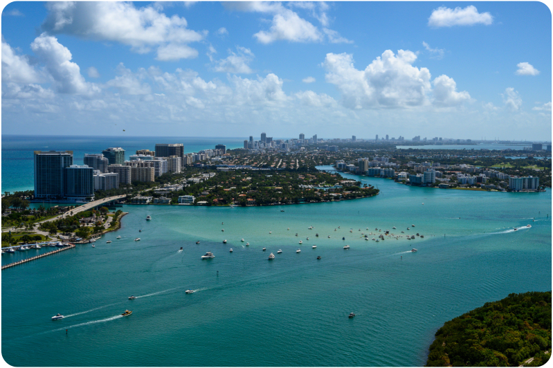 Aerial view of city skyline with blue water and boats, under a partly cloudy sky.