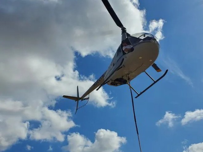 Helicopter in blue sky with clouds and a cable hanging down.