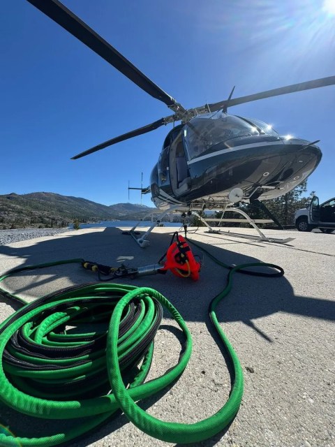 Helicopter on ground with coiled green hose and mountains in the background.