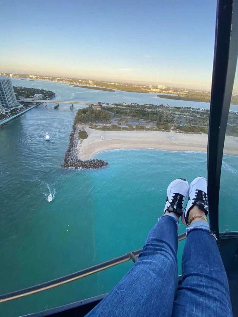 Person's legs in helicopter over beach and water on a sunny day.