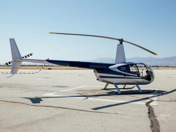 Small helicopter parked on an airstrip with mountains in the background.