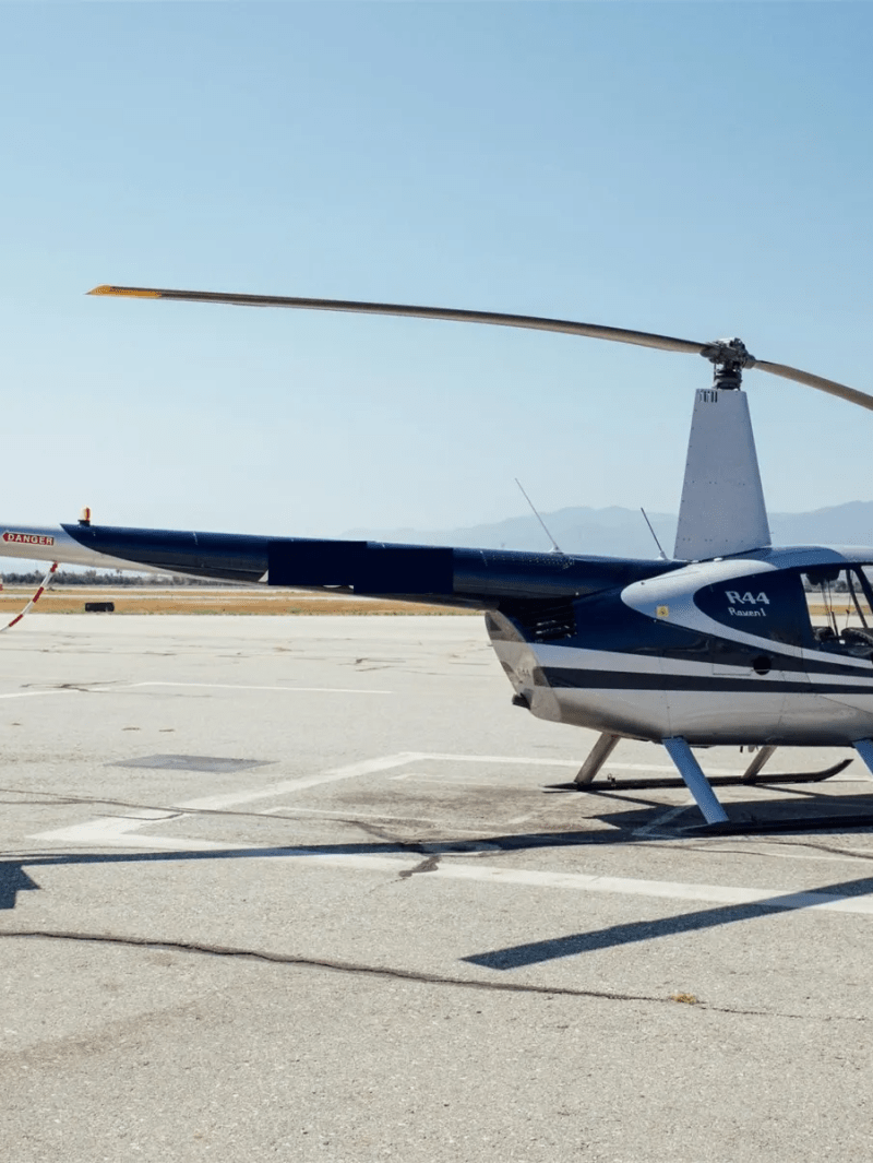 Small helicopter parked on an airstrip with mountains in the background.