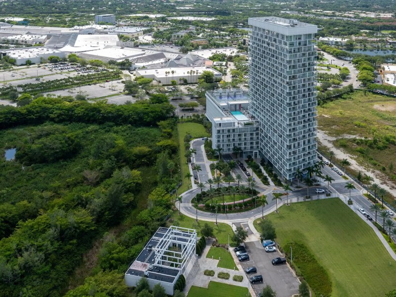Aerial view of a tall building, parking area, and surrounding greenery.