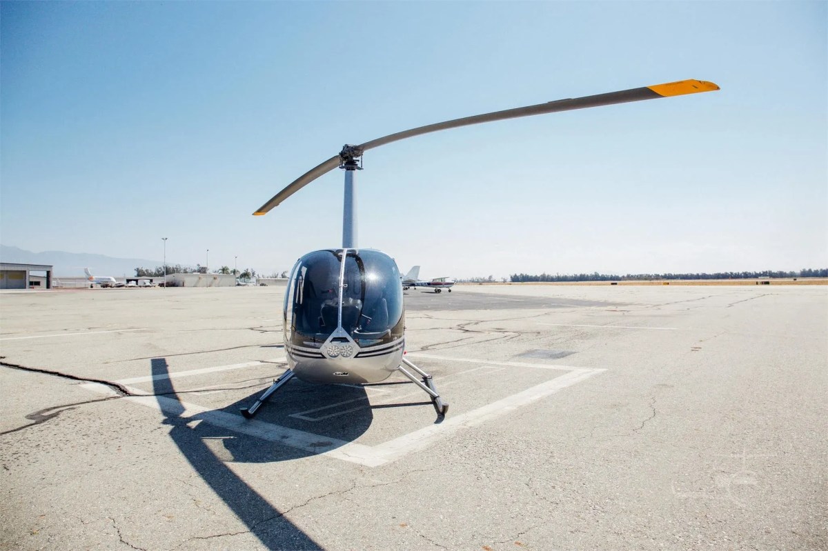 Small helicopter parked on sunny airport tarmac.