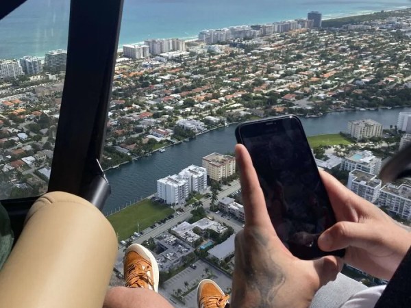 Person in helicopter photographing aerial view of coastal city with smartphone.