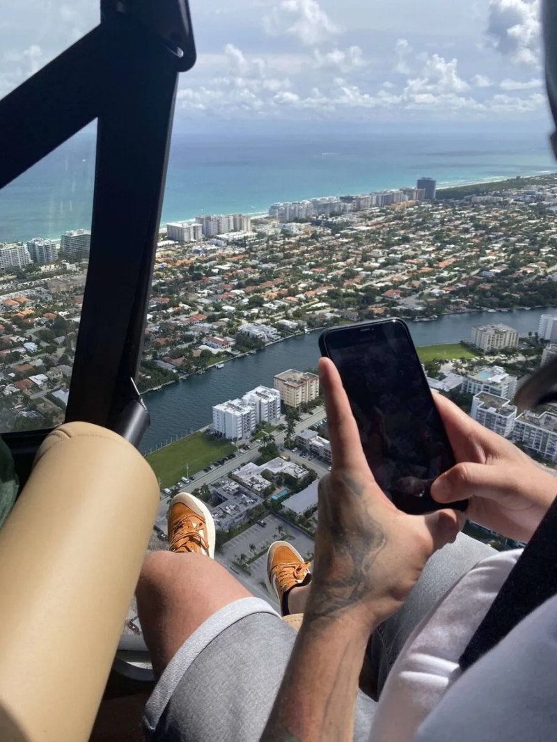 Person in helicopter photographing aerial view of coastal city with smartphone.
