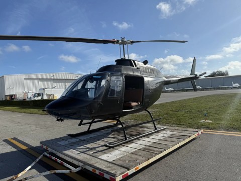 Helicopter on a wooden platform in sunny airfield, near hangars.