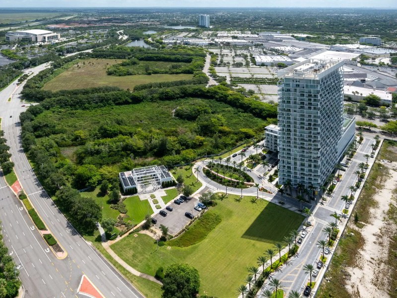 Aerial view of a tall building surrounded by greenery and roads in an urban area.