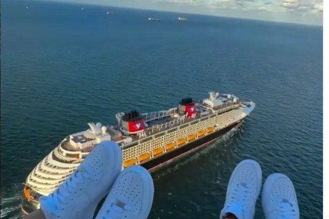 Two people with white sneakers above a cruise ship at sea.